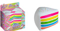A novelty squishy toy shaped like a slice of cake, shown next to its colorful retail packaging. The toy is white with rainbow-colored horizontal layers and small multicolored confetti details on top.