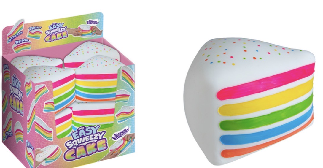 A novelty squishy toy shaped like a slice of cake, shown next to its colorful retail packaging. The toy is white with rainbow-colored horizontal layers and small multicolored confetti details on top.